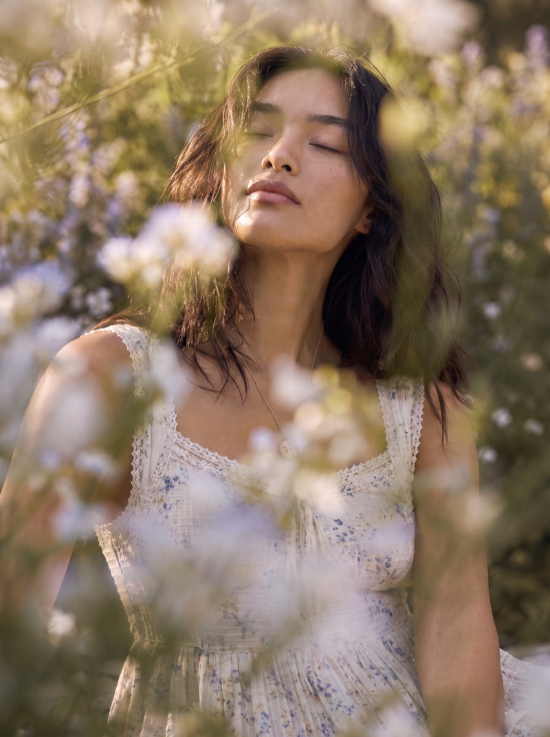 Previs frame: the model in a tiered white dress, eyes closed among the white blossom