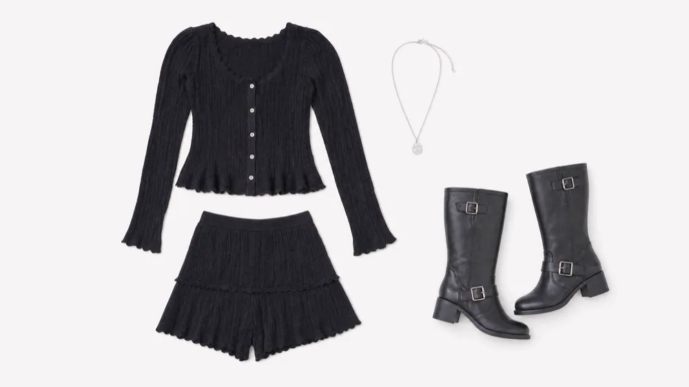The wardrobe laid flat on white: a black ribbed button-front cardigan, matching ruffled shorts, a silver pendant necklace and black leather buckle boots